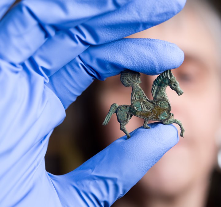 A person is holding a small horse brooch found at Arbeia.
