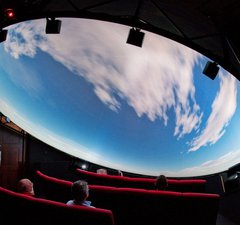 Visitors look up at a domed planetarium show. They are seeing clouds moving across a daylight sky