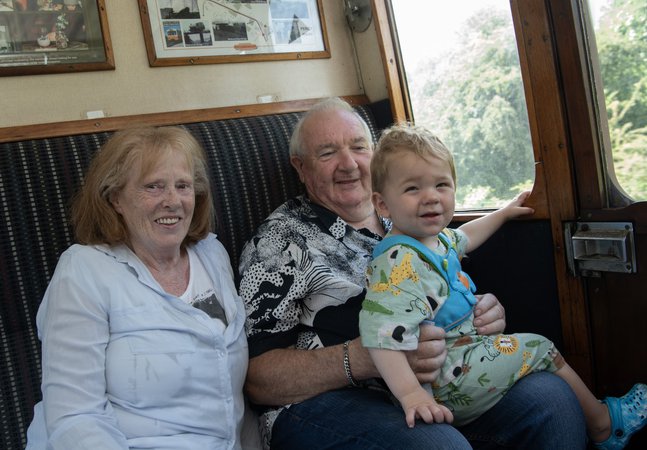 A family of three sit in a train carriage. They are smiling at the camera