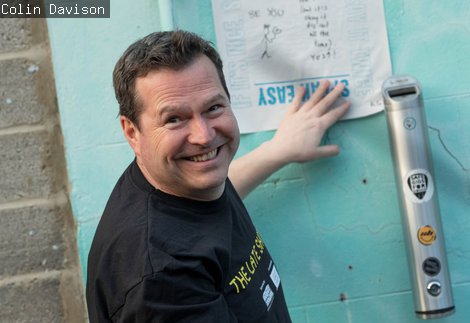 Photography of a male pasting a protest poster to a wall, looking back at camera and smiliing