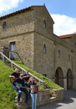 Four musicians sitting on a stone wall in front of a Roman style gatehouse