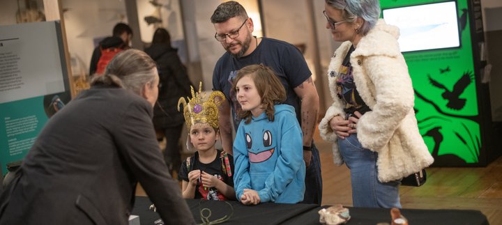 Two children and two adults are listening to a curator talk about museum objects.