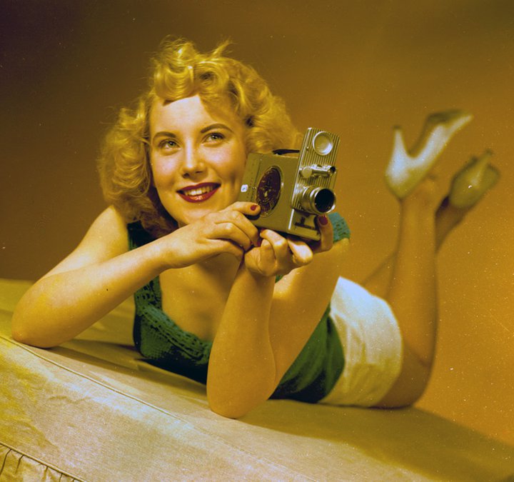 View of the model, Irene Warren, posing with a film camera for a Turners publicity shot, January 1957