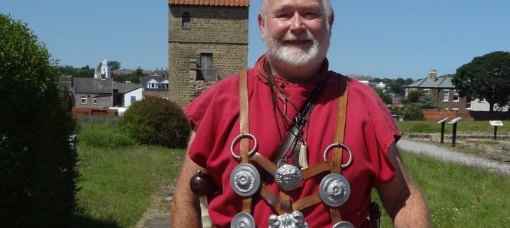Man in a red tunic, standing with the West Gate in the background