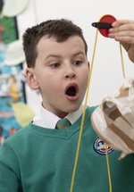 A child looks in awe at a homemade pulley system made of string and cardboard 