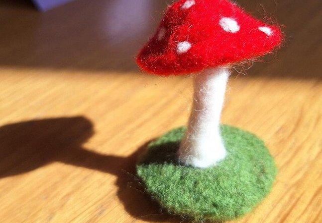 A photograph of a needle felted toadstool. The cap of the mushroom is red with white dots.