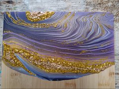 A photograph of an acrylic poured serving board. The decoration has purple swirls and gold decorations, inspired by geodes.