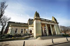 A photograph of the outside of the Shipley Art Gallery. The building is made of a yellow stone with columns in the front.