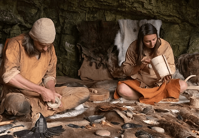 Two people are sat on the ground doing ancient crafts  