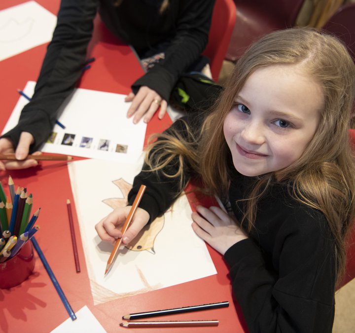 Girl sitting at a red table colouring in some paper