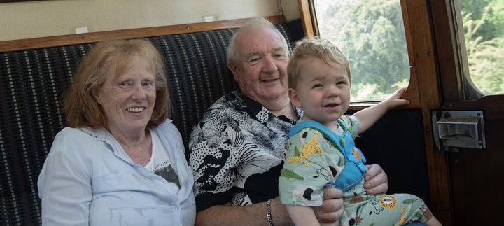 A family of three sit in a train carriage. They are smiling at the camera