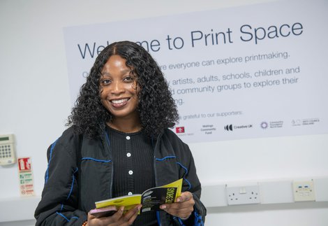 Girl holding a brochure, in front of a white wall with mural reading 'The Print Space'