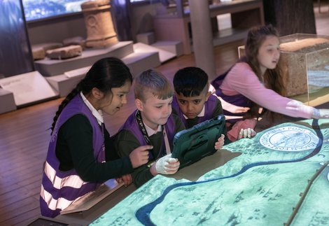 Children taking holding iPads next to a Hadrian's Wall model. 