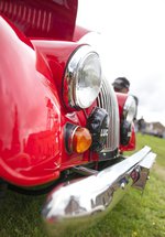 A bumper of a red vintage car parked on the grass in front of Woodhorn colliery. Men in the background are taking photographs