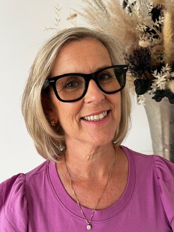 A person with short blonde hair and black rimmed glasses, smiling at the camera A person with short blonde hair and black rimmed glasses, smiling at the camera