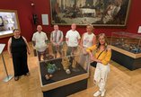 A group of six people standing around a glass display case with ceramic objects.
