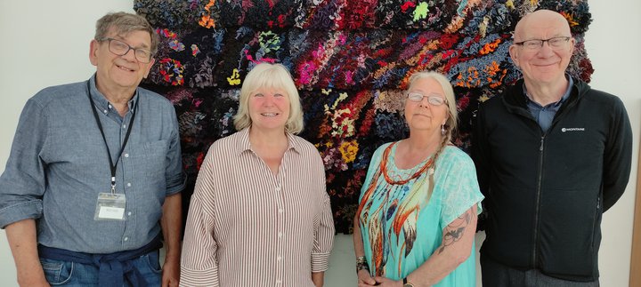 Four adults standing in front of a proggy mat on a wall