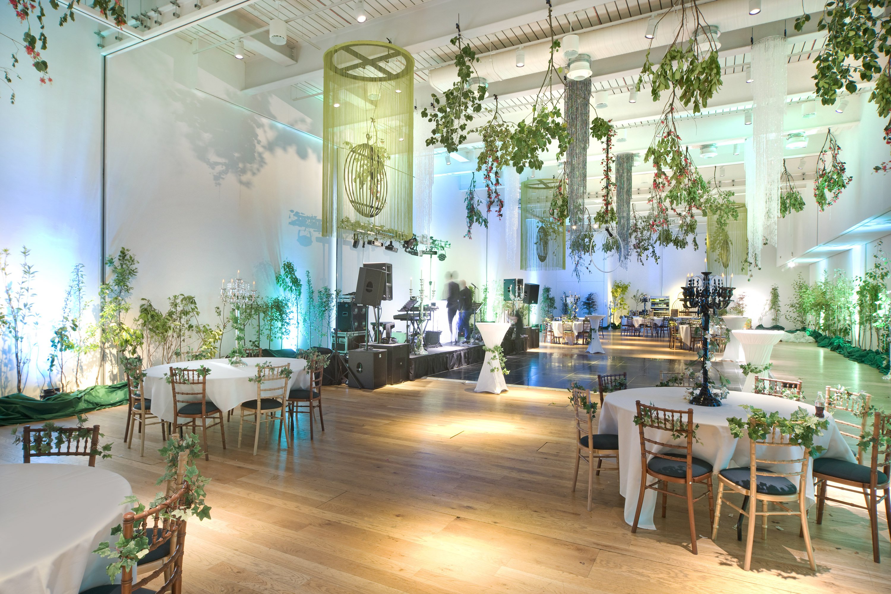 A large room with tables and chairs and greenery hanging from the ceiling.