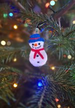 A photograph of a needle felted snowman Christmas decoration hanging on a Christmas tree.