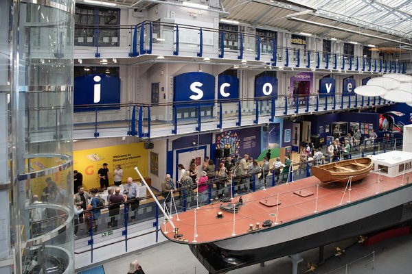 A wide image of an event around the Turbinia ship. Many people are standing holding drinks and having conversations in the museum