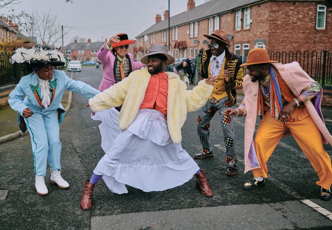 A photograph of five people in a circle dressed in colourful, formal outfits.