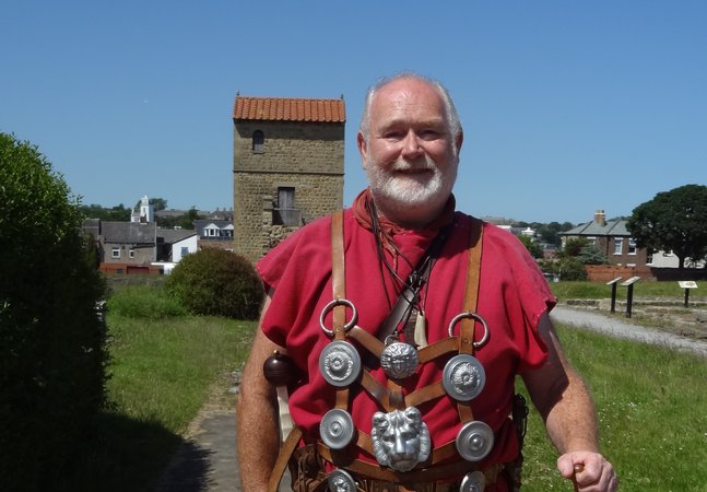 Man dressed in a red Roman style tunic holding a wooden staff