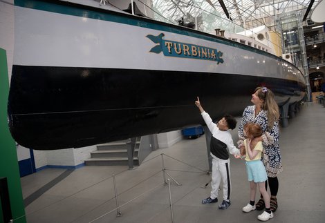 A parent and children look up at the Turbinia ship inside of Discovery Museum