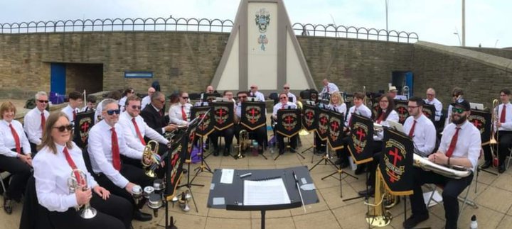 Members of a brass band sitting down outside with their instruments and music stands