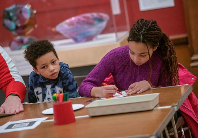A photograph of a girl with long braids and a young boy with short hair doing crafts. 