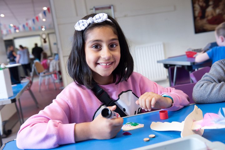 Young girl in pink top and white bow in hair, smiling, doing craft activity