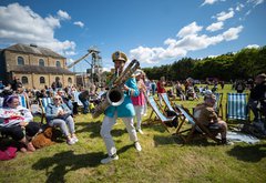 A man plays a saxophone to a group of people sitting on picnic chairs 