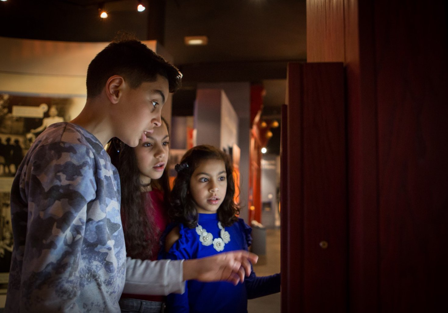 Three children look at a display case 