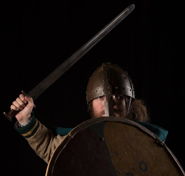 A man wears a viking helmet and holds a shield and sword.