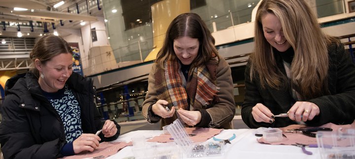 Three women crafting and smiling at Discovery Museum at night