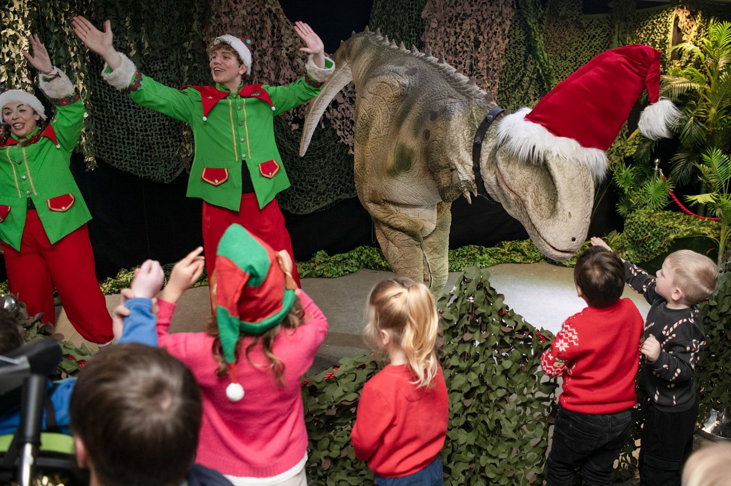 Two elves and a T-rex costumed actor are performing in front of children Two elves and a T-rex costumed actor are performing in front of children