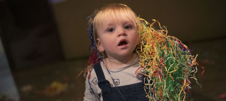 A toddler is covered in shredded coloured paper.