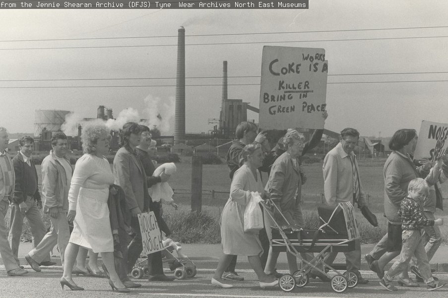 A black and white photograph of a group of adults and children marching with banners saying 