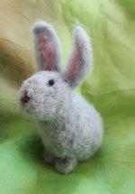 a needle felted bunny sitting on a green background