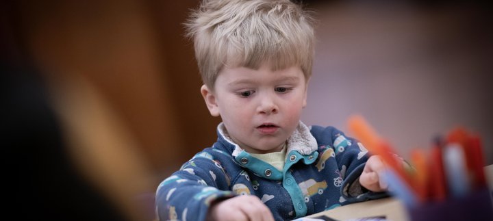 A child with short blonde hair sitting at a table and taking part in a craft activity