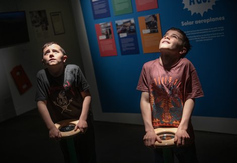 Two children are holding museum interactive wheels and looking up at the ceiling