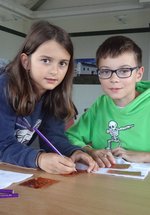 A boy and a girl embossing designs onto a copper sheet 