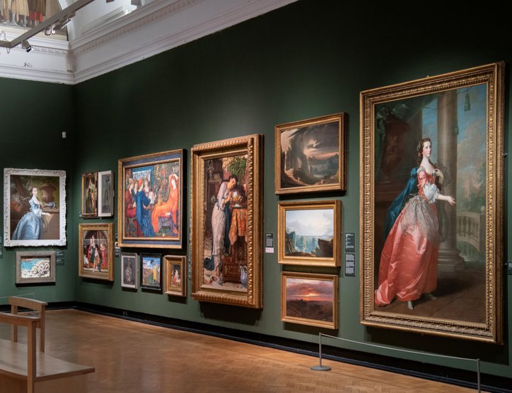 A photograph of the inside of the gallery. Oil paintings in frames hang on a green wall.