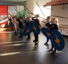 Group of school children learning combat skills with shields and spears