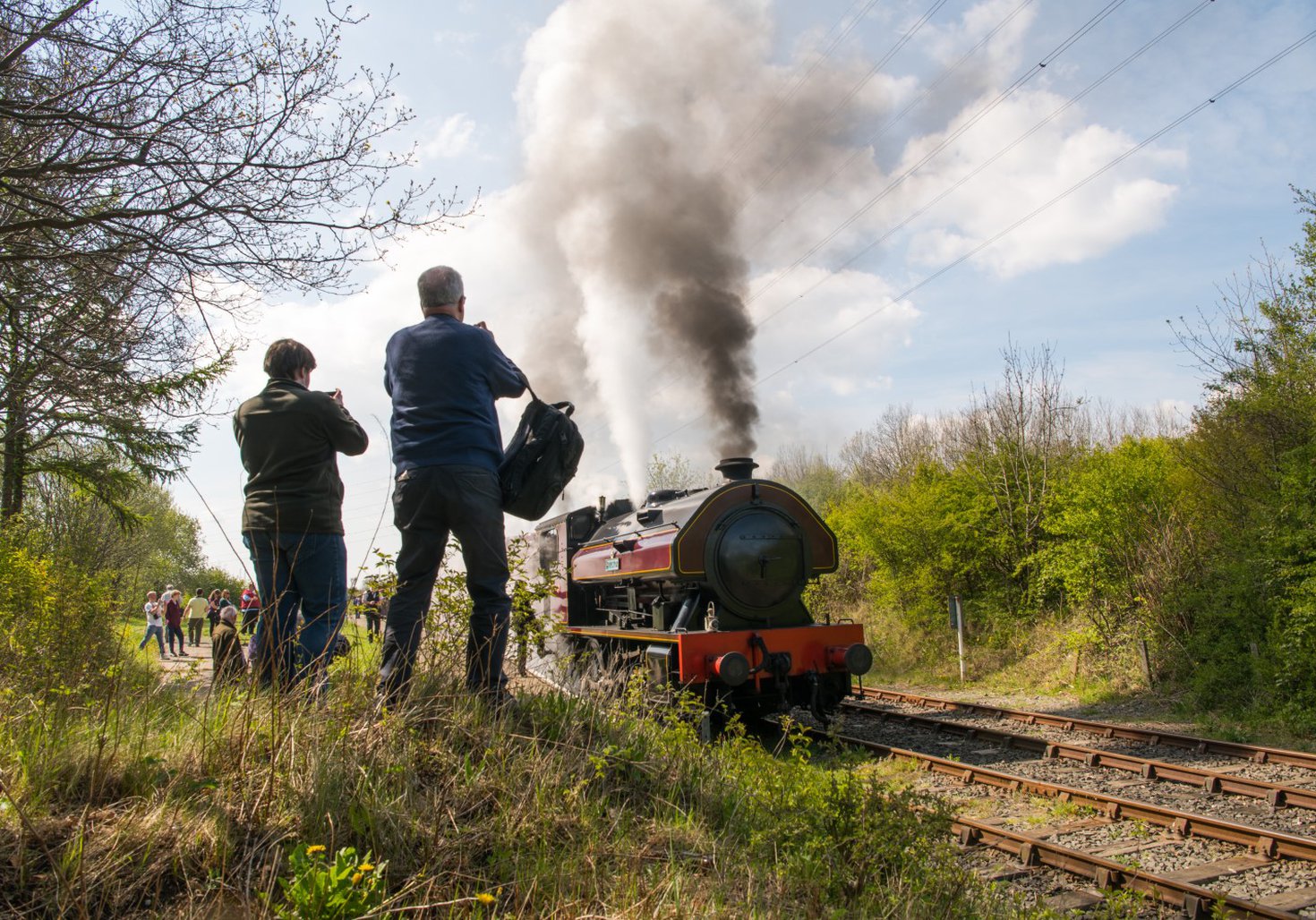 Two people photograph a steam train as it passes by 