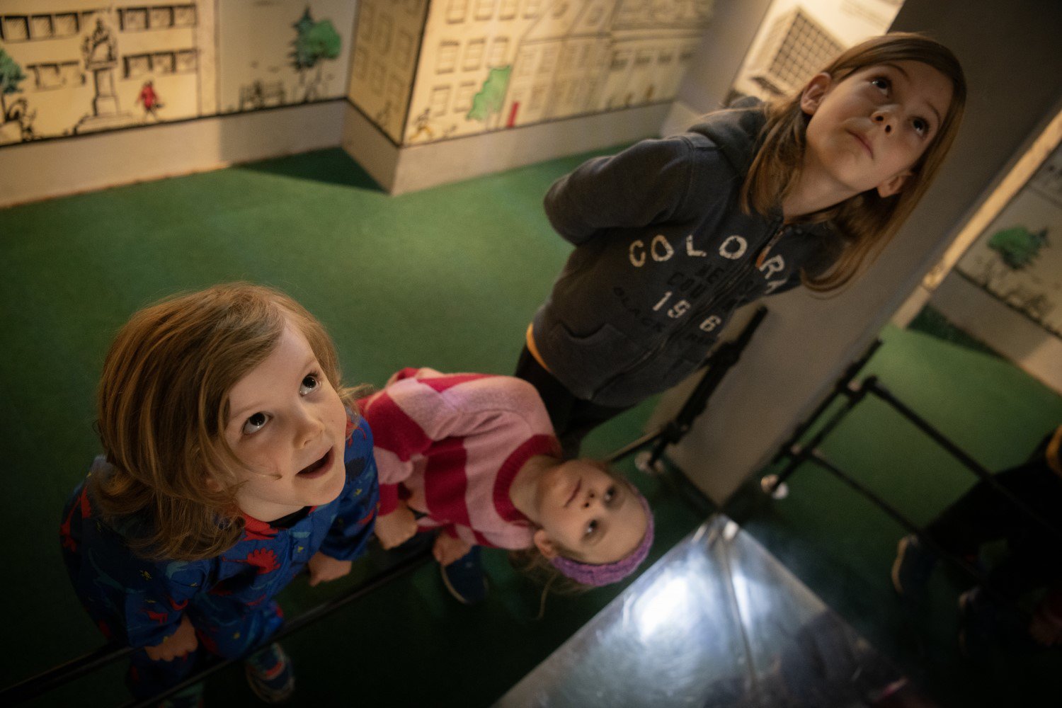 Three children in a museum exhibition look up at the ceiling. Three children in a museum exhibition look up at the ceiling.