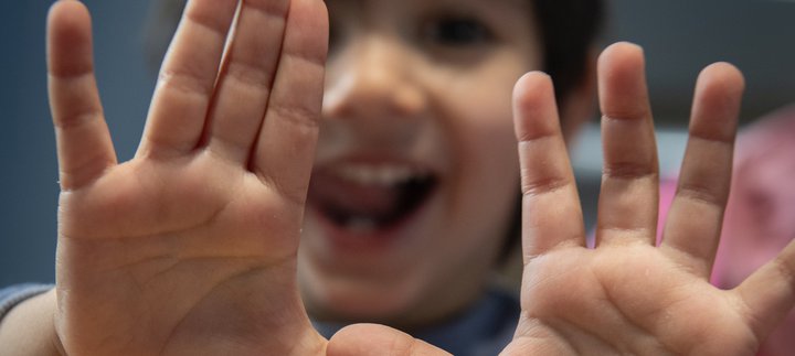 Little smiling boy holds up hands to camera