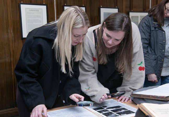 two women bending over to get a closer look at an archival ledger