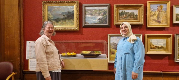 Two people standing smiling besides a glass display case in a gallery