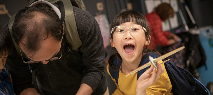 girl in Play Invent gallery holds her creation and laughs at camera