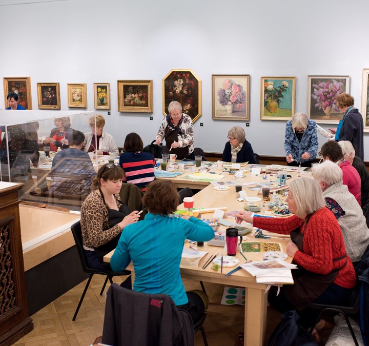 art class group sitting down at table painting in an art gallery
